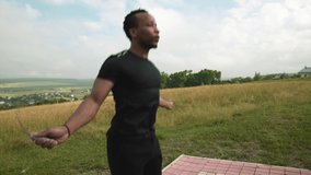 Concentrated african muscular guy in black sports wear training hard during everyday workout on fresh air. Handsome man using sports rubber equipment with green nature around