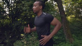 Side view of muscular afro american man with short haircut and concentrated facial expression wearing black t-shirt and doing morning exersices on fresh air. Cocept of combination of nature and sport