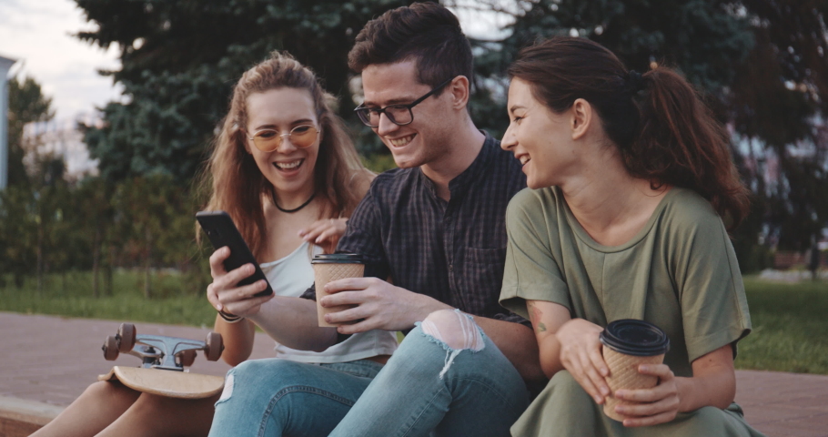 Happy smiling teenage friends laughing outside at something in smartphone or mobile phone. Three young multiracial people spending time together. Friendship, communication, youth and lifestyle concept | Shutterstock HD Video #1036137953