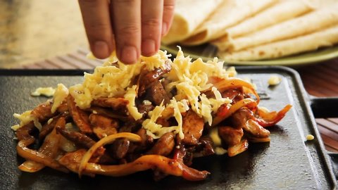 Adding cheese on top of the meats and vegetables for fajitas, mexican food