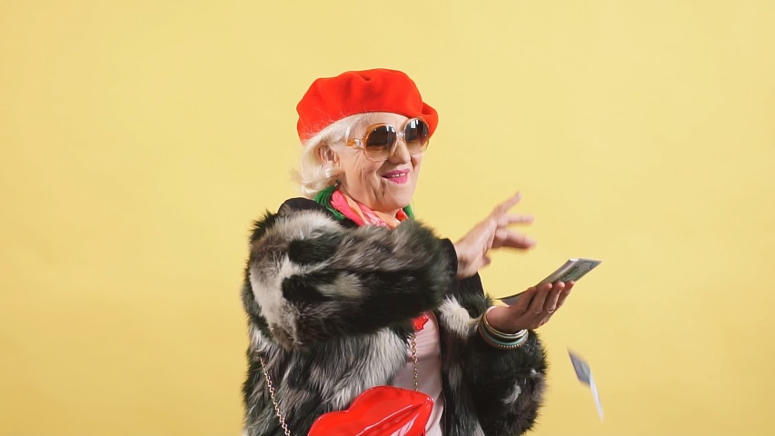 Rich elegant woman in fur coat and red cap throwing money, spending money on useless thing, isolated yellow background. studio shot Royalty-Free Stock Footage #1036143755