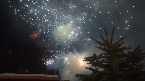 View of fireworks and salute from a clearing located in the French Alps in Courchevel. Fire show. Night. Colored lights in the sky above the mountains in Europe. Festive salute. Forest.