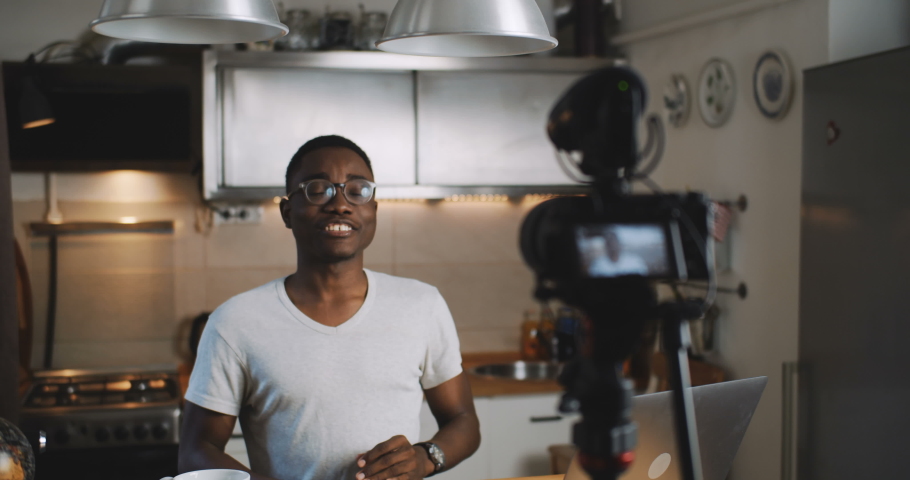 Happy young smart black blogger man filming new vlog video with professional camera in kitchen at home slow motion. Royalty-Free Stock Footage #1036150409