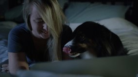 Young woman in bed with her dog streaming movies on her laptop