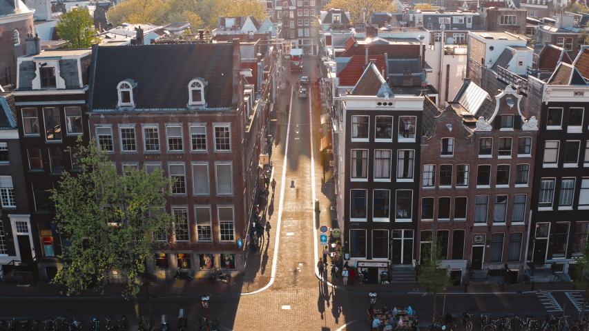 Amsterdam, Netherlands: flying over roofs of houses along narrow street with bridge above narrow canal, traffic on road