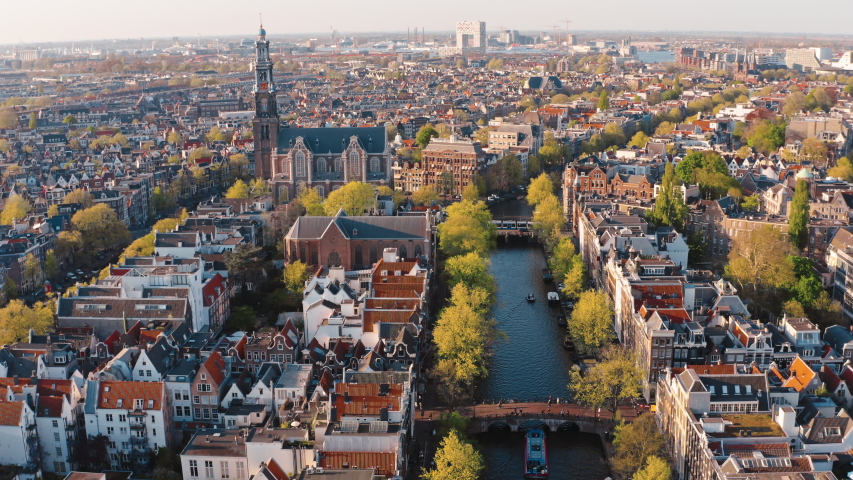Amsterdam, Netherlands: drone view of Westerkerk church and narrow canal with bridges and boats traffic