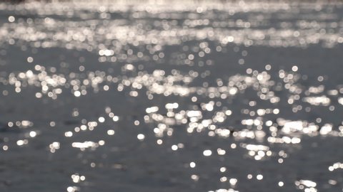 Abstract nature. Blurred bokeh sun glare glistening on wavy water surface.