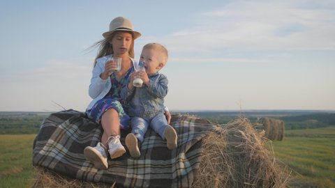 Little brother and older sister sitting on a haystack in a field at sunset and drink milk.