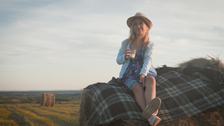 Pretty girl in blue dress drinking milk on a haystack in the field. Child on a summer picnic. | Shutterstock HD Video #1036162058