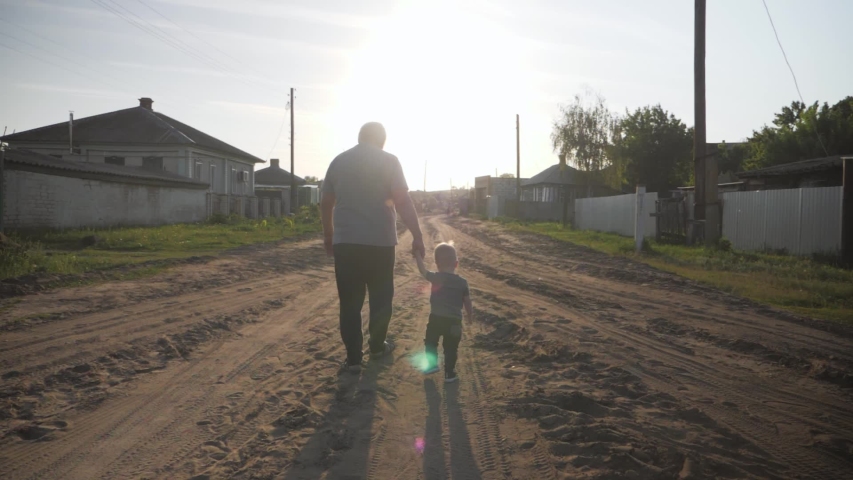 Two generations silhouette of a mature grandfather and little grandson to go at sunset.