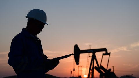 Silhouette of a oilfield worker monitoring crude oil pump at sunset.