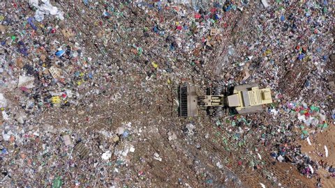 Top down aerial footage of a Municipal Solid waste Landfill during collecting, sorting and pressing work, with a massive flock of White birds passing by.