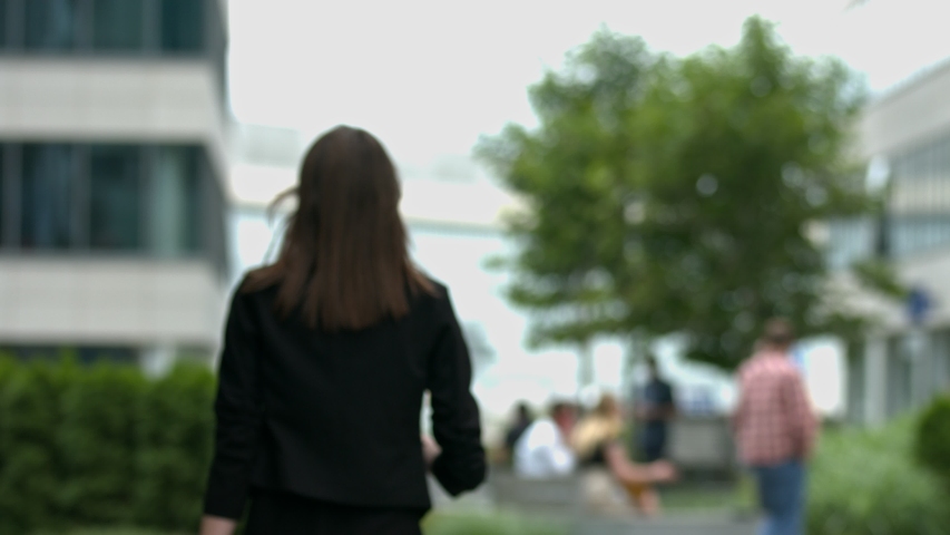A woman with long brown hair walks away from the camera, in a modern urban setting
