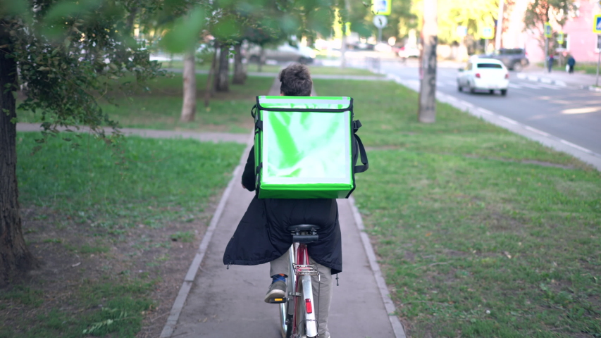 delivery man with green backpack rides a bicycle through the city with food delivery. Royalty-Free Stock Footage #1036173893