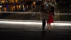 A man and a woman are dancing on a bridge in the center of Moscow. Against the background of Red Square and the Moscow River. Night video in the Zaryadye park.