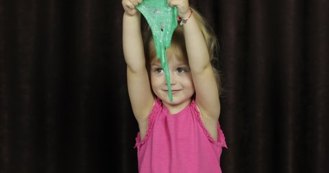 Child having fun making green slime. Kid playing with hand made toy slime. Funny kid girl. Relax and Satisfaction. Oddly satisfying blue slime for pure fun and stress relief. Dark background