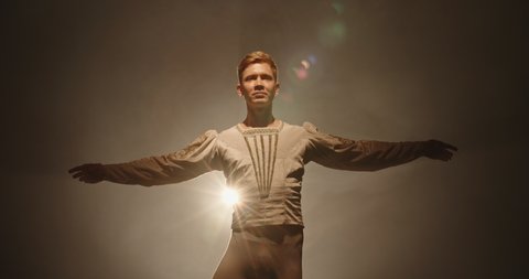 Handsome caucasian male ballet dancer performing pirouette and spinning on stage, wearing white tights, spotted by searchlight and isolated on black background 4k footage