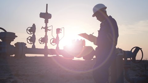 Silhouette of a oilfield worker monitoring crude oil valves manifold at sunset.