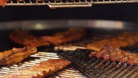 Portions of spicy marinated beef ribs grilling on a rotating grill in a close up view as they pass the lens at a catered event or restaurant