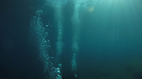 SCUBA divers swim towards a deep a ship wreck in very dark blue water.  Their bubbles are the only thing well illuminated from the distant sun.