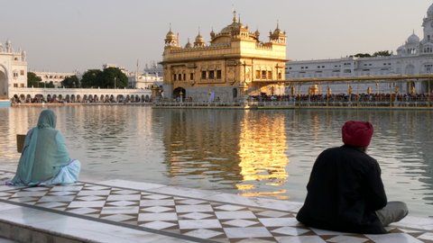 a sikh man and woman sit beside the sacred pool at golden temple in amritsar, india