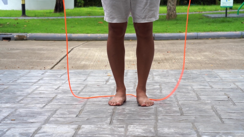 Shoeless Asian male  jumping rope at the park. 
