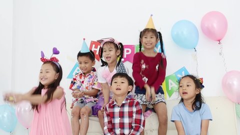 Group of happy asian kids raised up and enjoy throwing colourful confetti with friends in birthday party