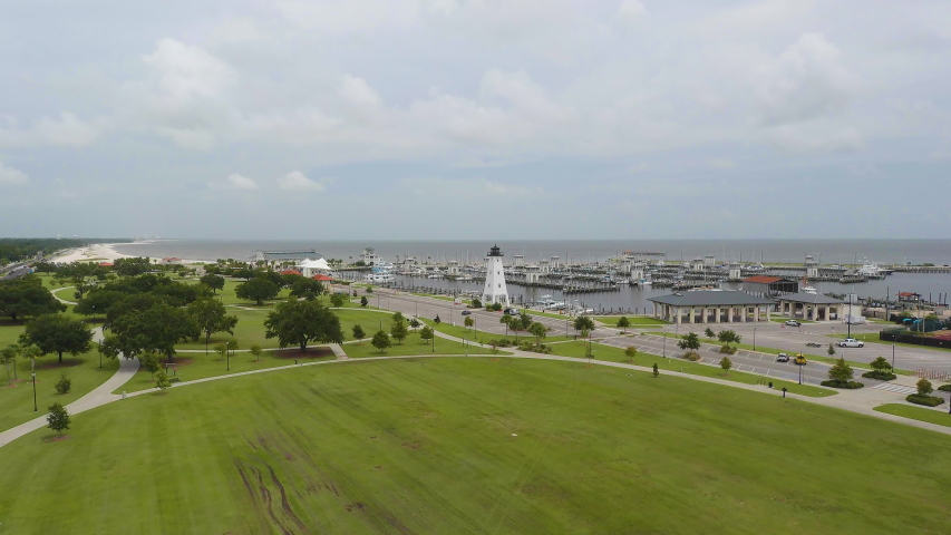 Aerial view of a lighthouse on the edge of a boat dock at a park on the edge of the ocean. Filmed in 4k 60fps and slowed to 24fps (23.976).