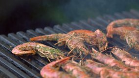 Grilled whole fresh pink prawns seasoned with herbs on the griddle in a close up view as someone turns them with tongs as they cook