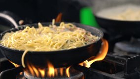 pan of savory pasta in a creamy sauce simmering over hot flames at a restaurant in a close up view on the food