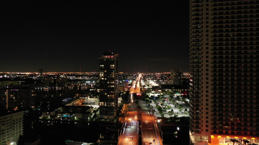 Aerial night time dolly through buildings over streets in Miami