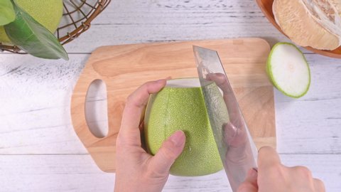 Young asian woman is cutting fresh pomelo to eat at home kitchen on bright white wooden table and chopping board, top view, overhead view, lifestyle.