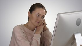 Blonde girl with pink pullover looking at monitor of computer watching video on gradient background.