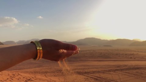 Slow Motion shot of sand falling through a woman's hand in the Wadi Rum Desert, Jordan. Shot at sunset with mountains in the background.