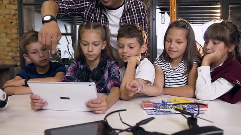 Group of five caucasian children with korean man using tablet pc studying computer programming in computer class. Education, science, technology, children and people concept. Slow motion