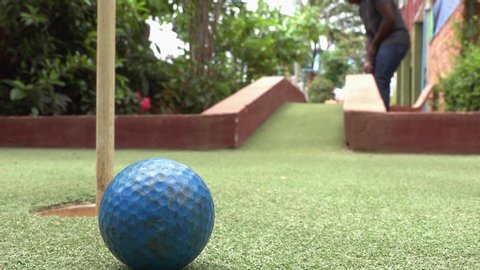 Close and Low Shot of a Golf Ball Being Chipped Over an Obstacle and Hitting the Pin on the Green at the Mini Golf Course