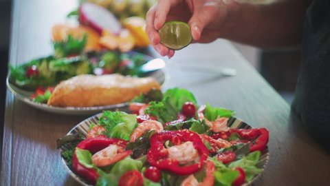 Close up of hand squeezes lime on Vegetable Fresh Salad. Food Healthy Meal, Mediterranean Diet. Slow Motion. Fresh colorful salad with shrimp.