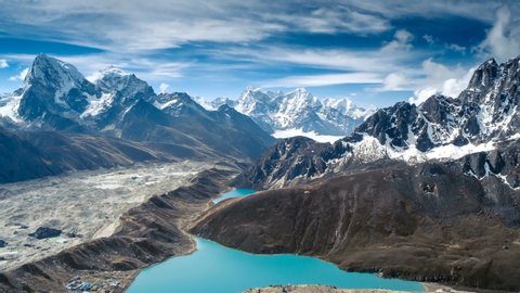 Calm Blue Gokyo Lake surrounded by bare rocky hills against high mountains with snow on slopes upper view. Travel, landscape, holiday, recreation. Himalaya, Nepal. Slow motion, parallax, time lapse 4K