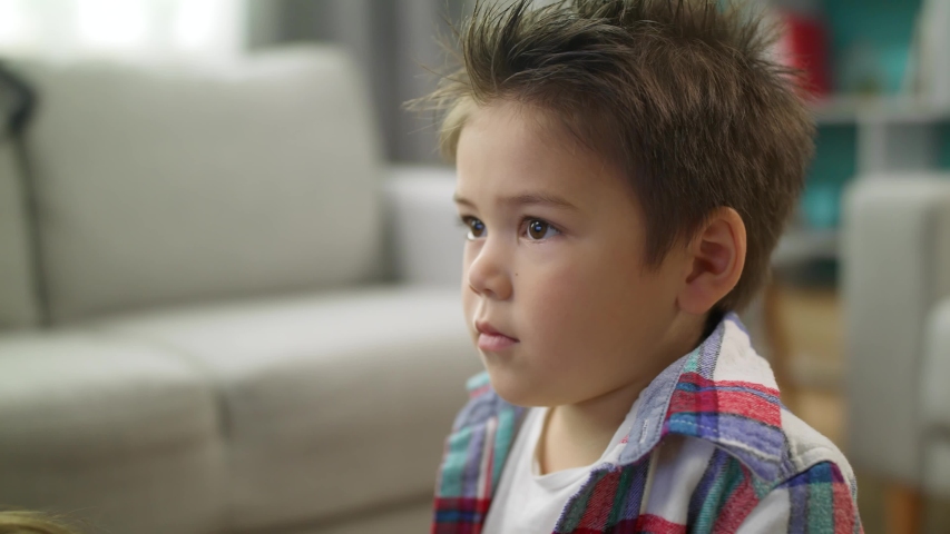 Little boy carefully watches cartoons on TV siting on the floor in living room