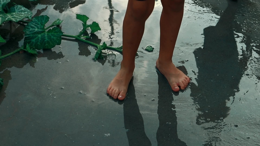 lonely child insolation outcast depression child abuse young boy shadow silhouette playing sliding his barefoot side to side in a water puddle sky and clouds reflection childhood fun and games