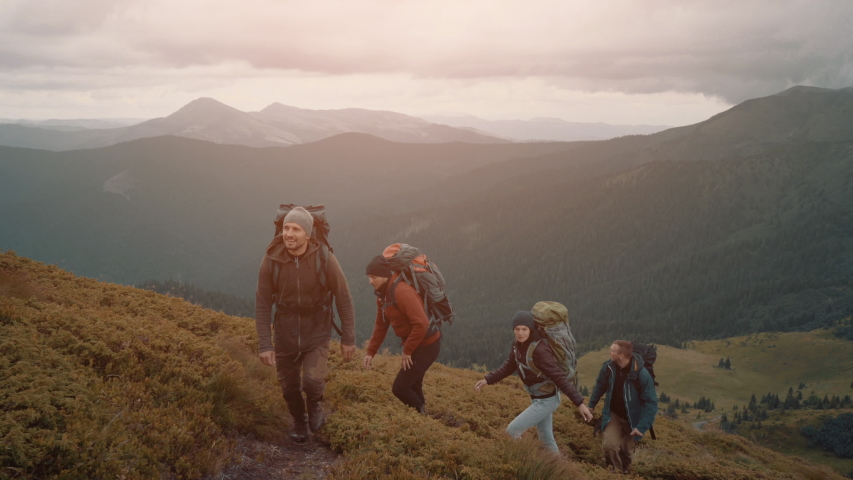 The four active people with camping backpacks walking down in a mountain