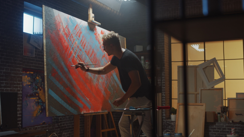 Talented male Artist Works on Abstract Oil Painting, with Broad Strokes of Paint Brush he Creates Modern Masterpiece. Dark and Messy Creative Studio where Large Canvas Stands on Easel Illuminated | Shutterstock HD Video #1036270001