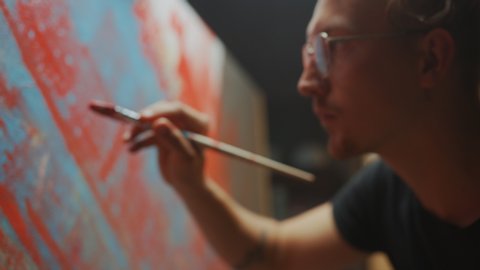 Portrait of Talented Artist Working on Abstract Painting, Uses Paint Brush To Create Daringly Emotional Modern Picture. Dark Creative Studio Large Canvas Stands on Easel. Side View Closeup Arc Shot