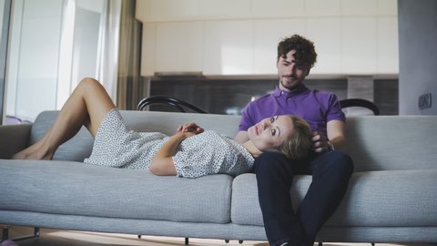 Millennial couple in love relaxing together on sofa at home. Happy couple looking to each other and laugh. Focus on girl