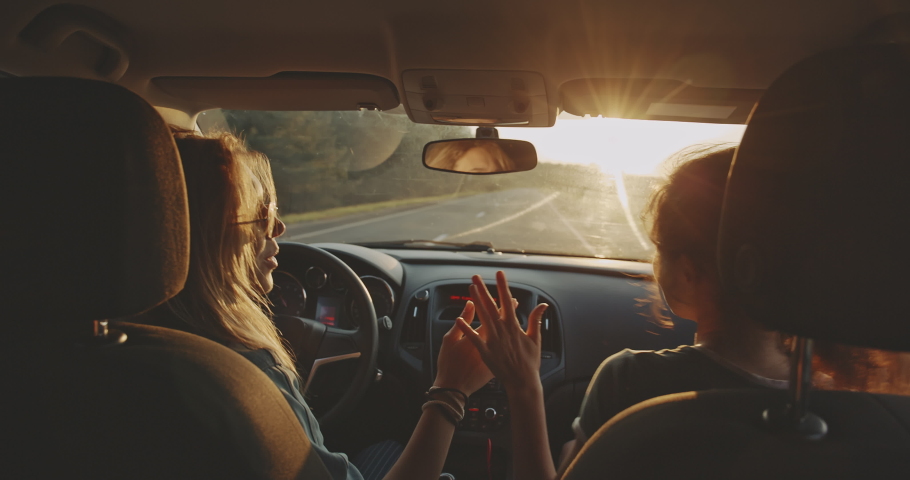 Two happy female friends enjoying traveling in the car. Sitting in front seat and having fun on a road trip. Girls driving car and dancing. Concept of youth, friendship, holidays and vacation. | Shutterstock HD Video #1036275515