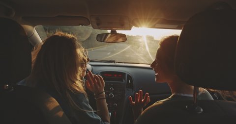 Two happy female friends enjoying traveling in the car. Sitting in front seat and having fun on a road trip. Girls driving car and dancing. Concept of youth, friendship, holidays and vacation.