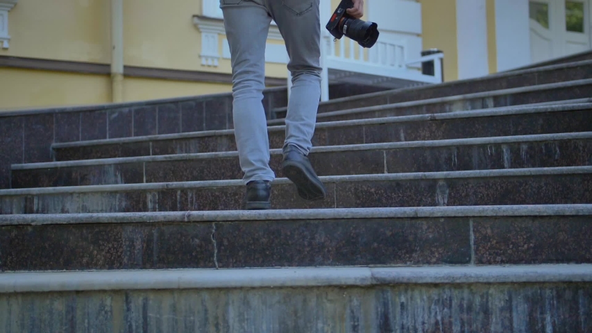 Rear view of a tourist legs with a camera climbing the steps of a historic building. Slow motion. Casual clothing. Concept person interested in history and architecture.