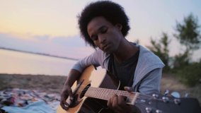 Handheld view of African man playing the guitar and singing on the beach