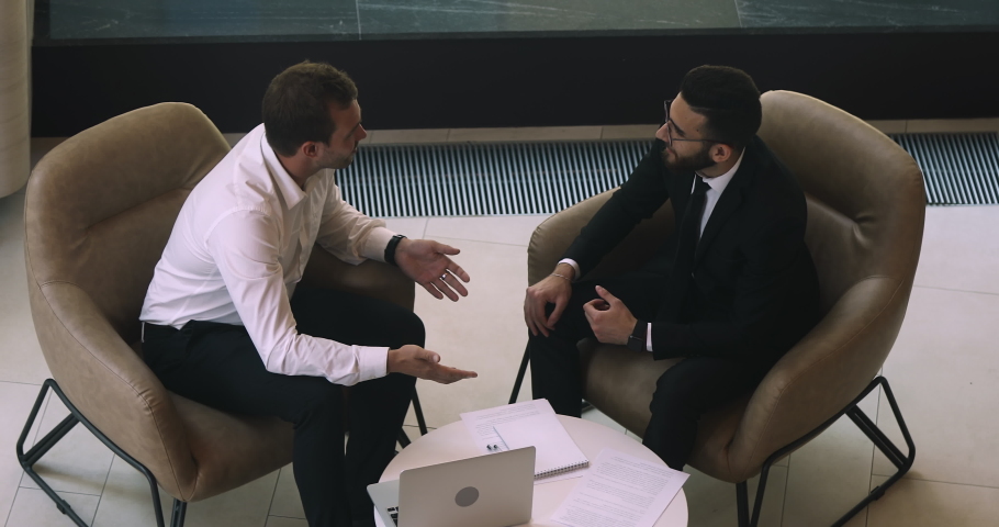 Happy diverse male business partners talk handshake sit on chair at office meeting, two businessmen shake hands making business agreement establish partnership investment deal concept, above top view Royalty-Free Stock Footage #1036278413