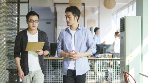 two young asian businessmen discussing business while walking in office of small company
